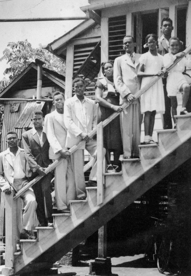 Black and white photograph. Six men, a woman, and two children stand on a flight of outdoor steps leading up to a house. Most of them rest their hands on the railing.
